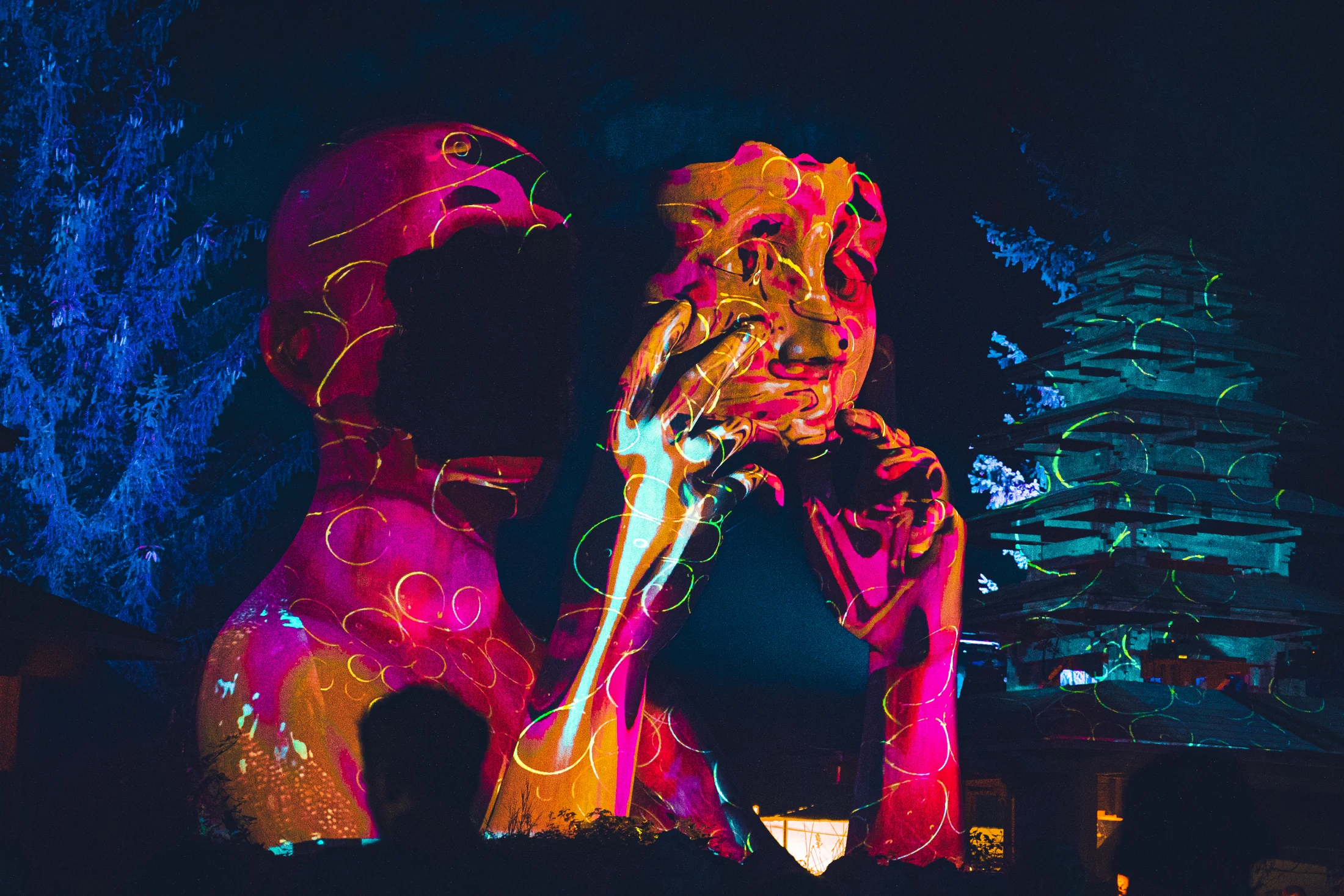 Brilliant pink, orange and blue microscopic imagery projected onto sculptural forms, with visitors silhouetted in front.