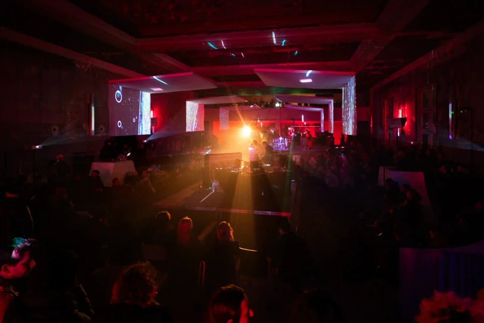 Visitors gather throughout the Wilhelmine hall beneath floating screens, warm light and microscopic projections.
