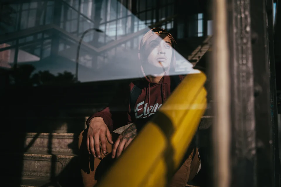 A seated person viewed through layered reflections in a window.