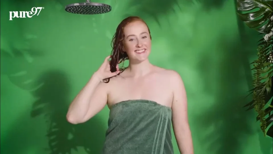 A smiling woman holding her wet hair against a green set in the pure97 Get Ready film.
