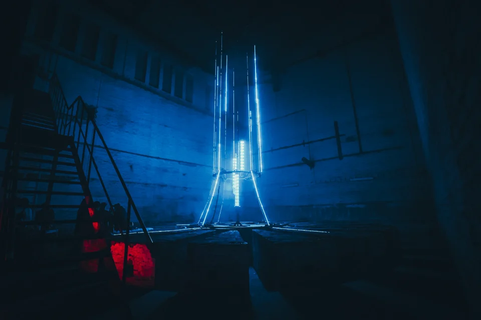 A tall blue light installation glowing inside a dark industrial space at Monopol Berlin.