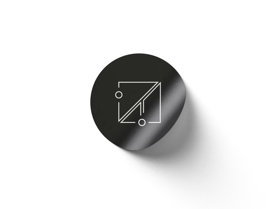 A fine geometric white monogram on a dark circular sticker.
