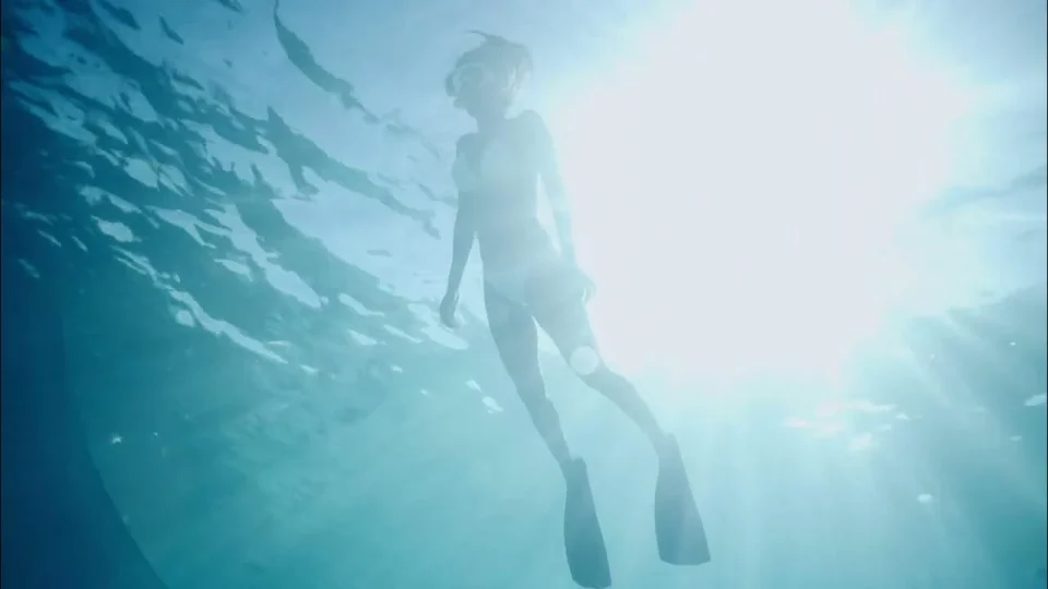 An underwater silhouette suspended beneath an illuminated turquoise sea surface, from Nomade.