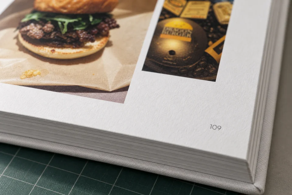 An extreme close-up of the printed food photograph, matte paper texture, page number and finely layered book edges on the cutting mat.