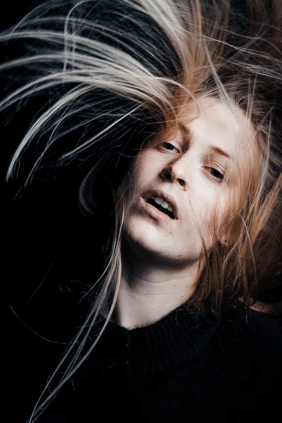 An intimate portrait with wind-blown blonde hair crossing the face and catching the light.