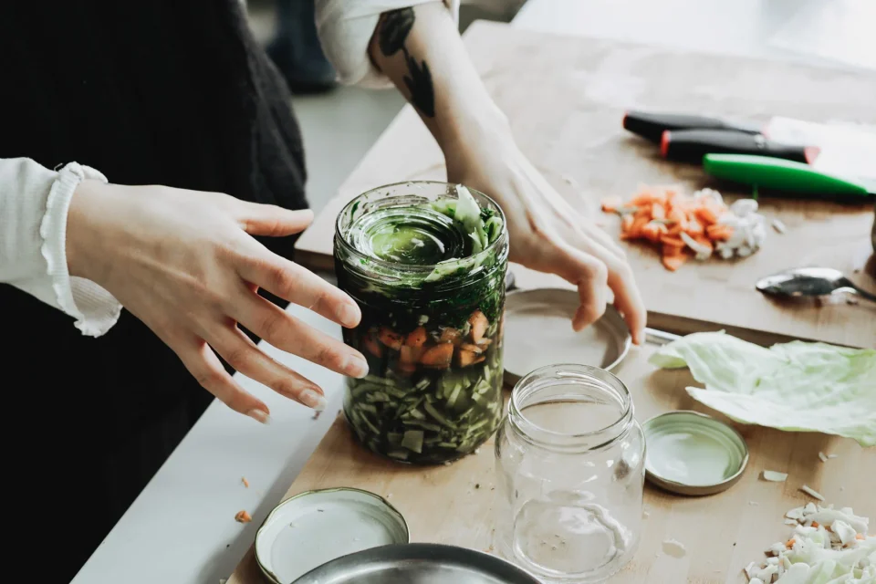 Existing Sinnkraut workshop photograph showing hands preparing a jar of vegetables and wild herbs.