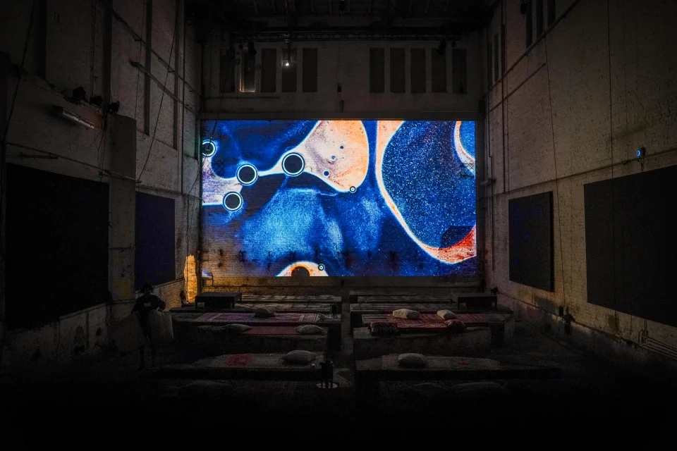A large screen of blue, cream and orange microscopic patterns at the end of an industrial room.