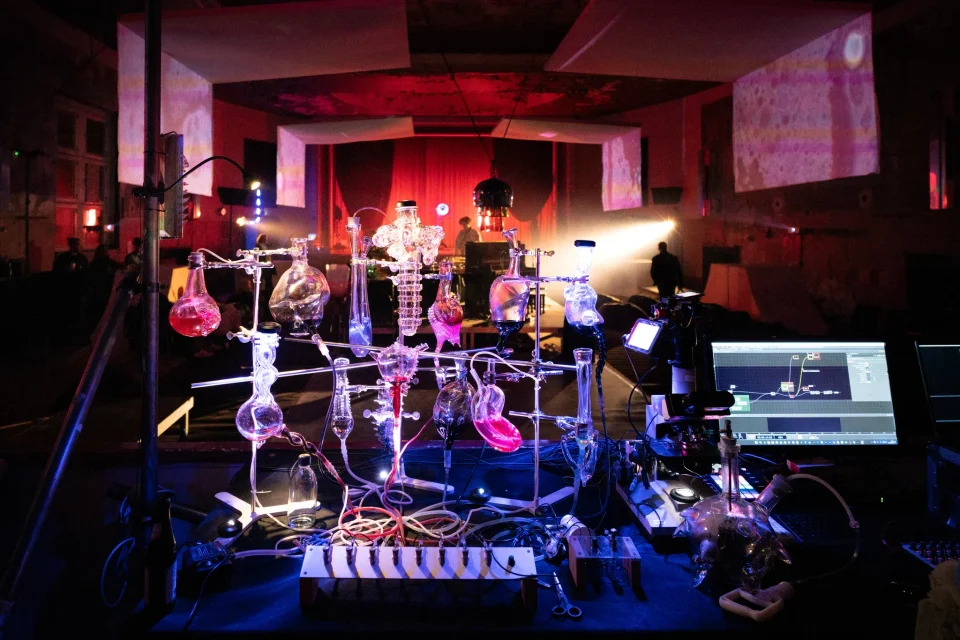 Illuminated glass apparatus, cameras and a computer stand in front of the projection-filled Encounters hall.